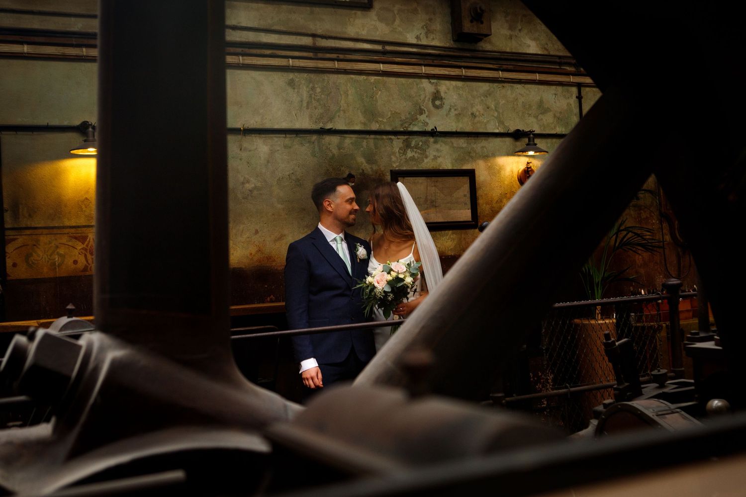 An artistic wedding portrait framed through industrial elements in low light.