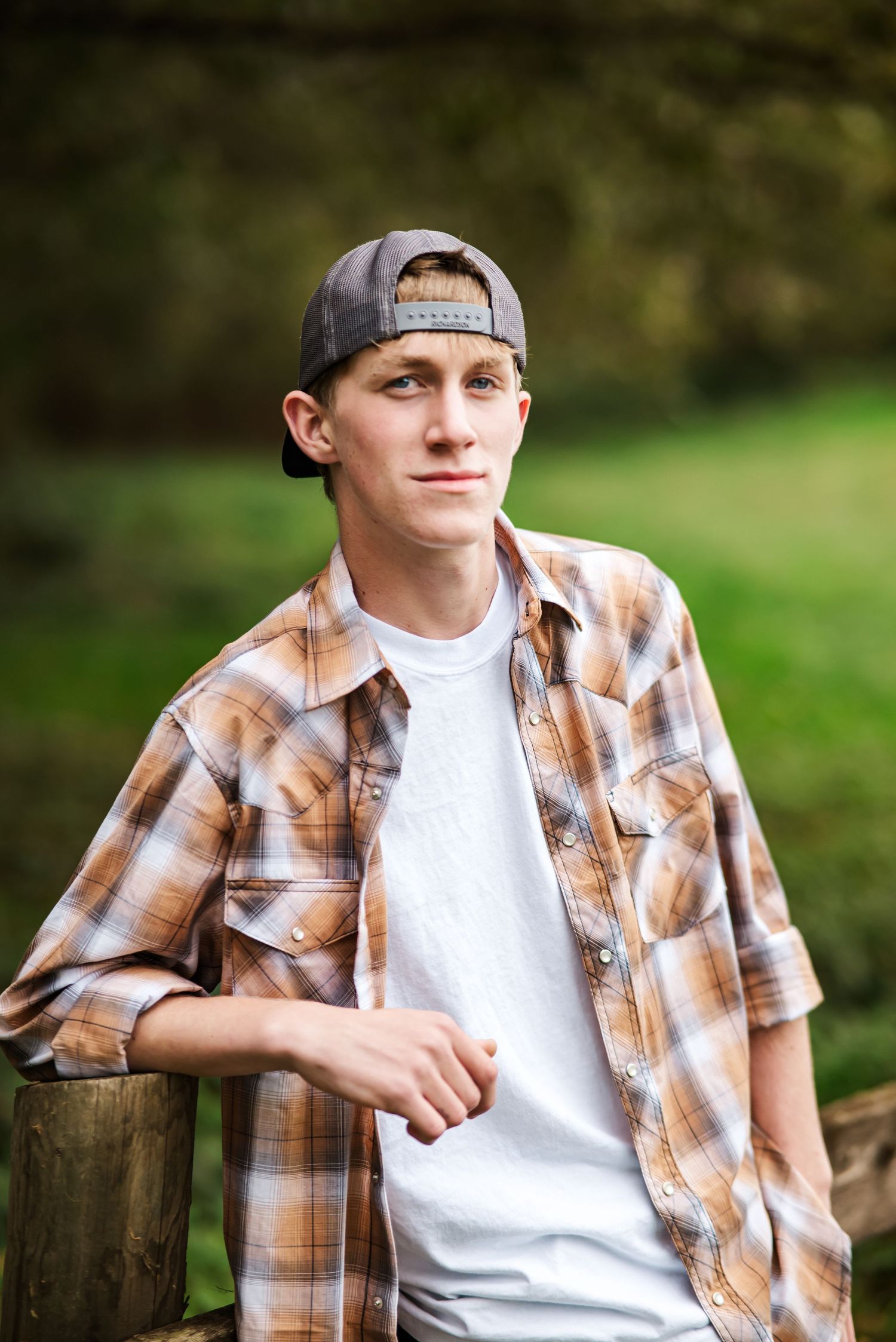 senior guy with backwards cap leans on fence and offers camera a slight smile