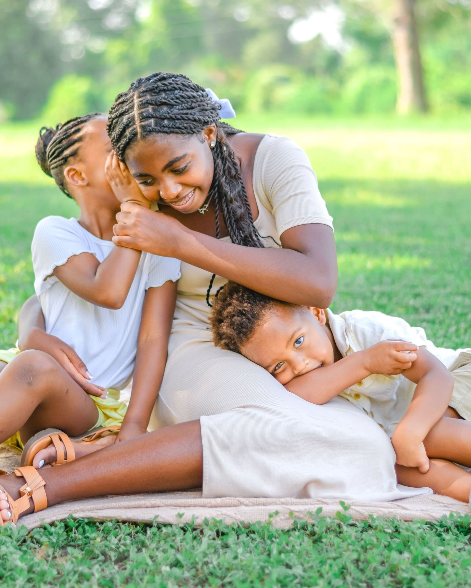 Parent and children sharing intimate playful moment while relaxing on grass in park.
