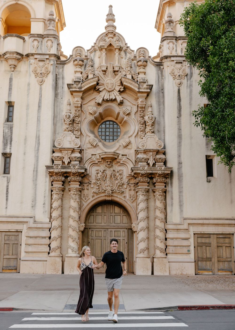 A couple shares a romantic moment in front of an ornate Spanish Colonial style church facade.
