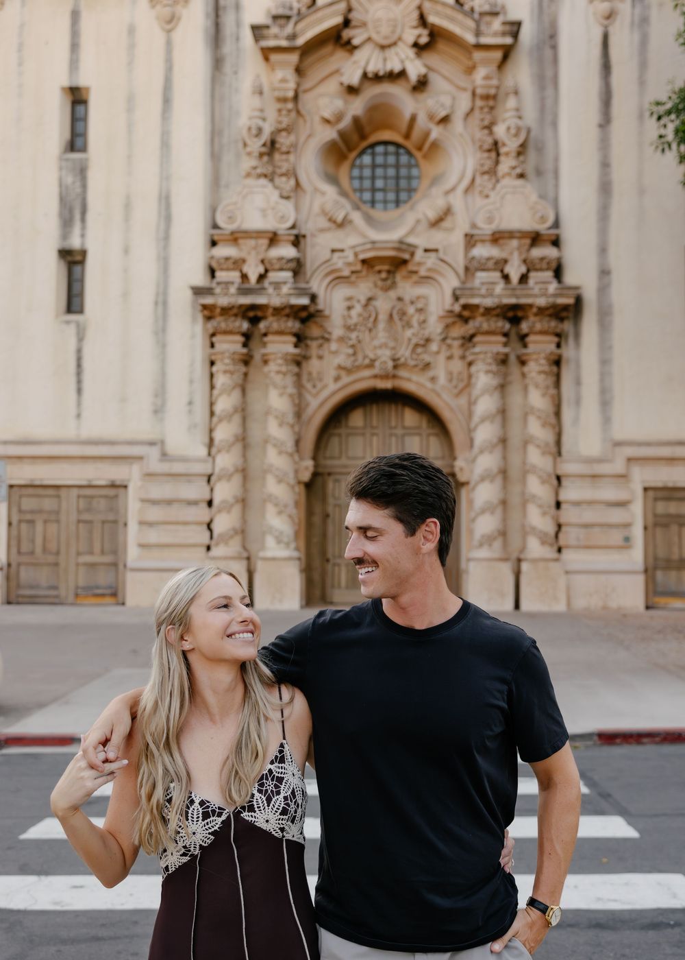 Couple shares tender moment in front of ornate baroque church facade with detailed stone carvings and architecture.