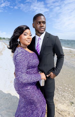 A couple poses together on a beach, with one wearing a sparkly purple dress and the other in a black suit.