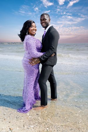 Couple poses in formal attire during beach photoshoot with purple sequin dress.