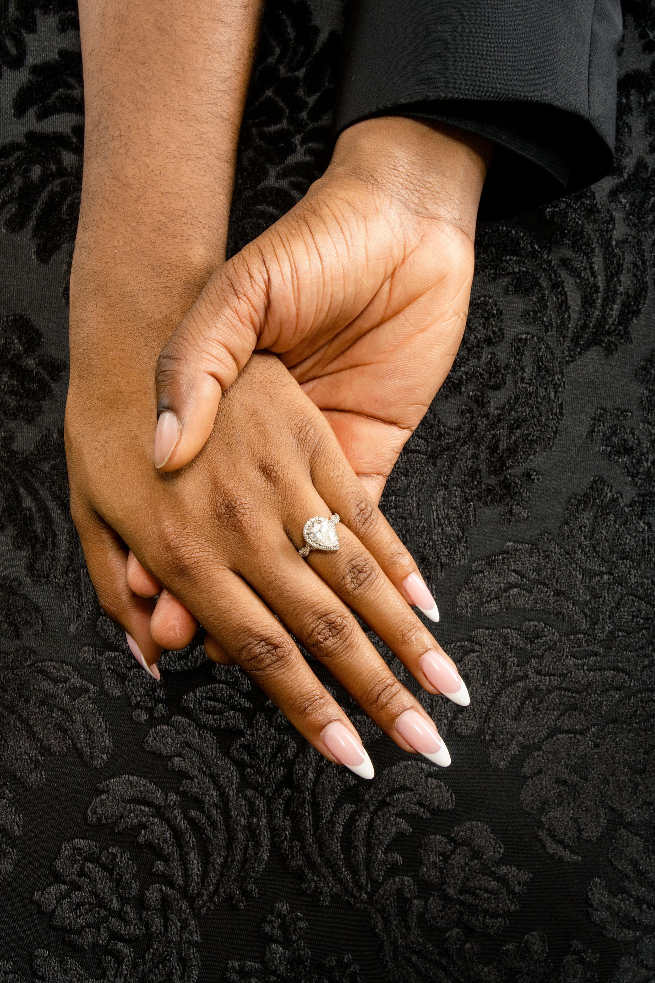 Close-up of hands showing off engagement ring against dark textured background.