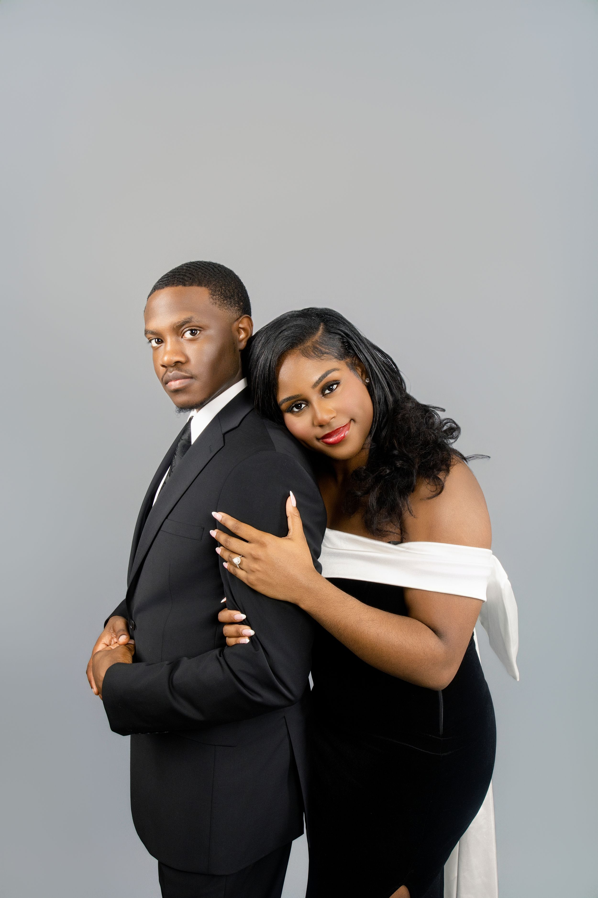 Couple embraces while wearing contrasting black and white formal wear during studio photoshoot.