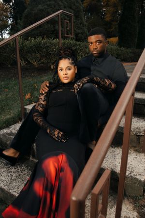 Couple in black attire pose together on outdoor steps during autumn.