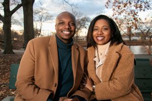 Couple in stylish winter coats sitting together on park bench during autumn.