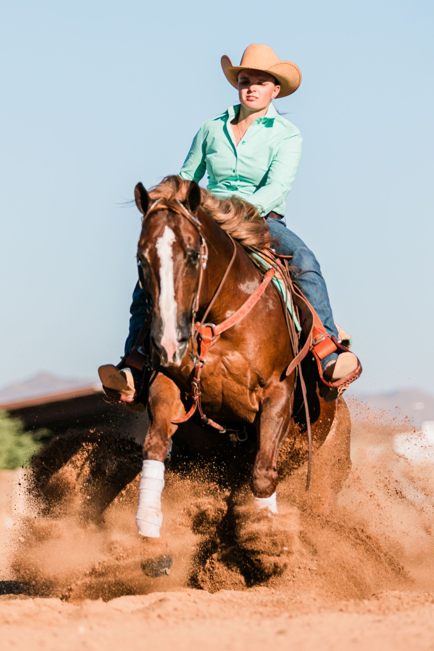 A horse and rider perform a sliding stop maneuver in a dusty arena, creating a dramatic cloud of red dirt.
