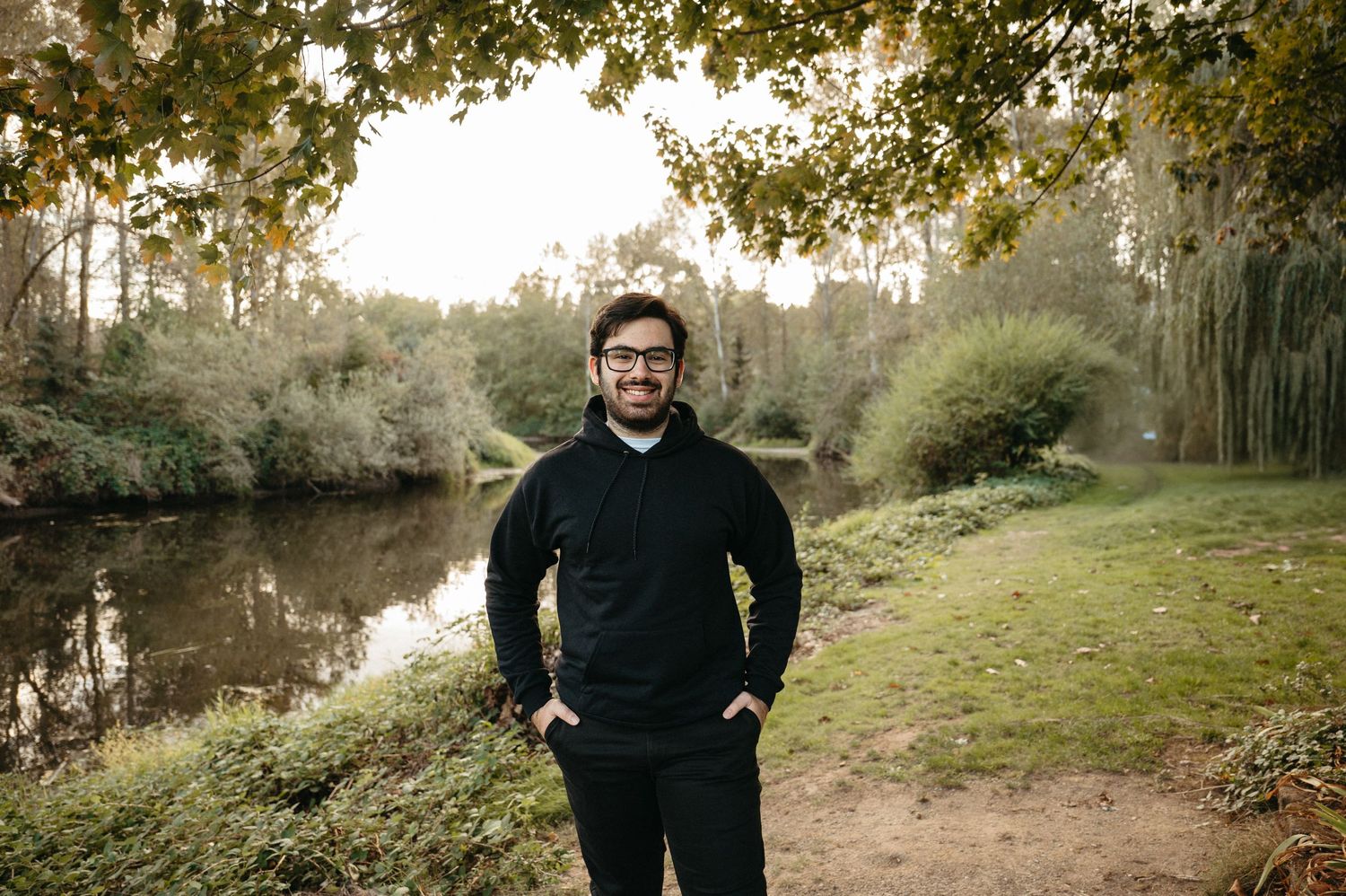 Person in black sweater standing on path next to tranquil pond at dusk.