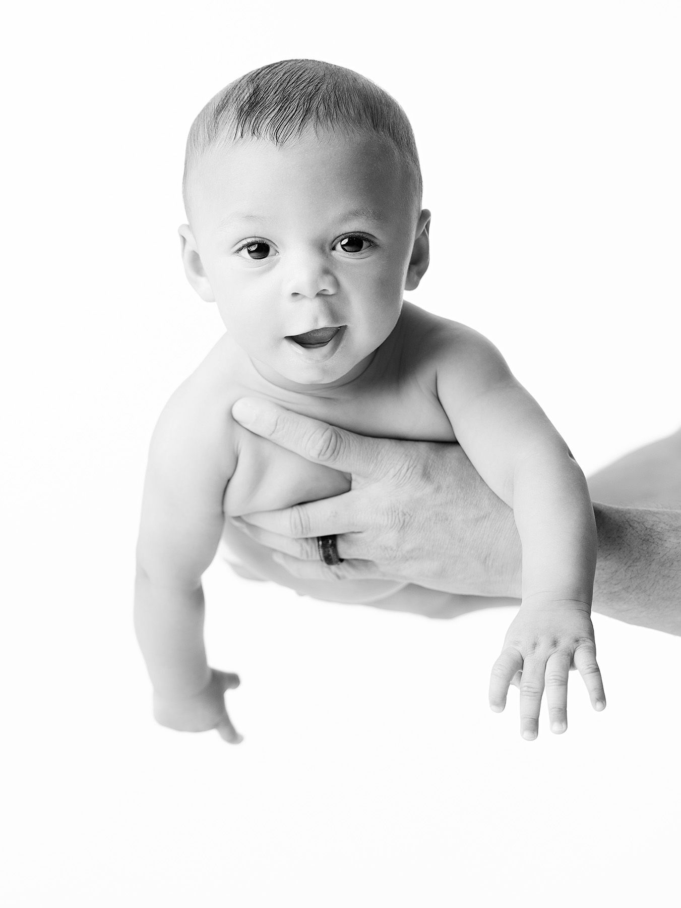 A baby sits in a curved wicker basket wearing blue pants against a neutral brown backdrop.