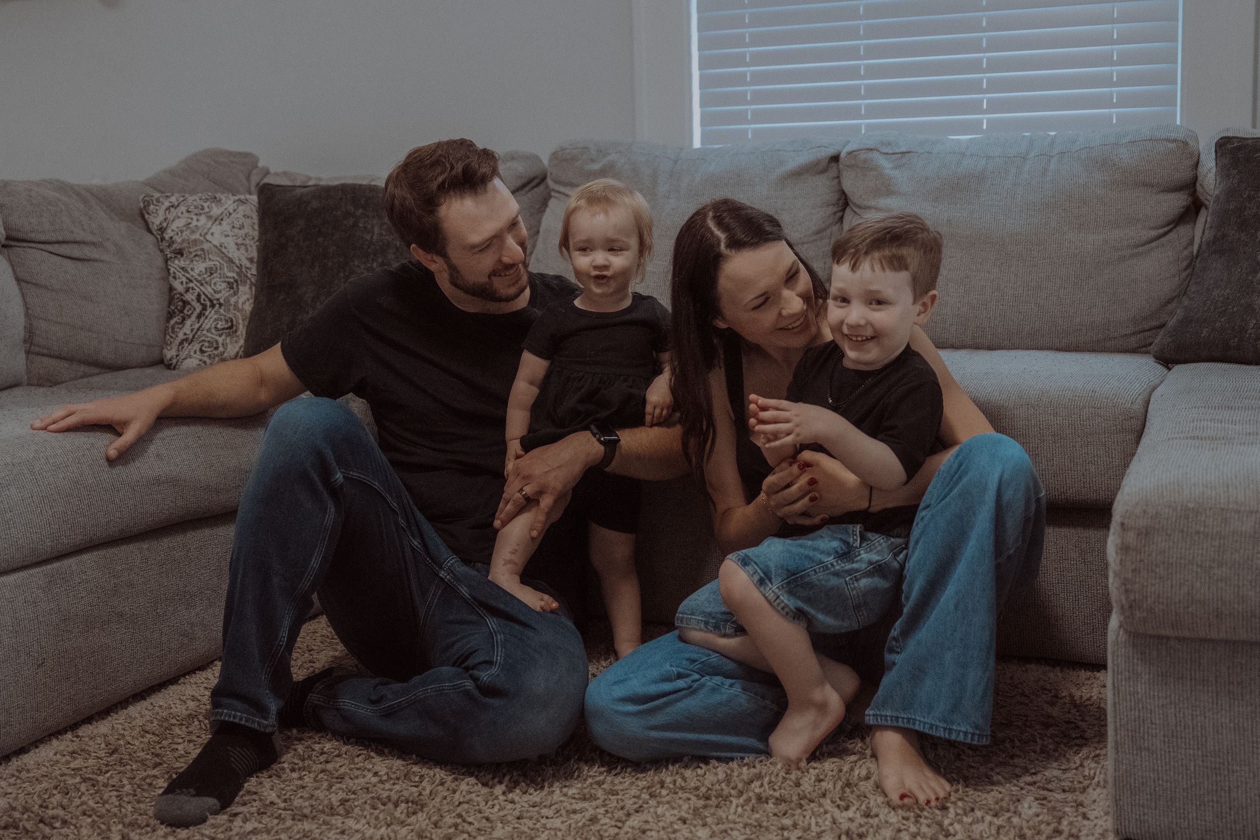 Family sitting together on gray couch sharing intimate moment in casual home setting.