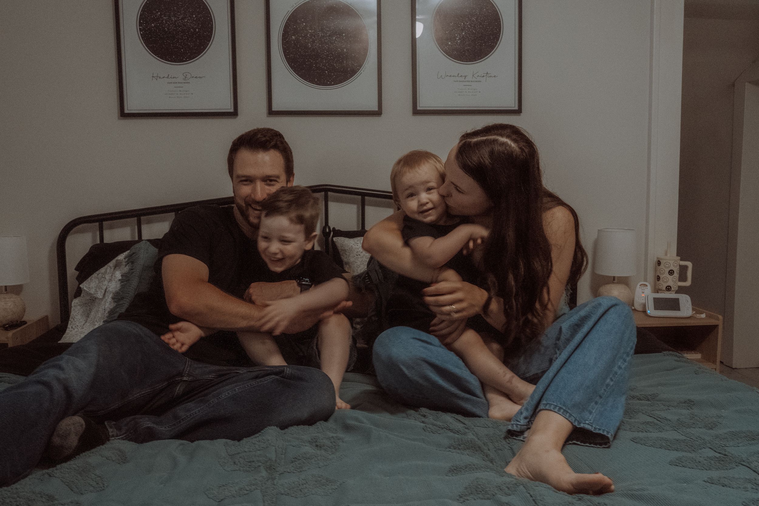 Family relaxing together on bed with decorative moon phase prints hanging on wall in background.