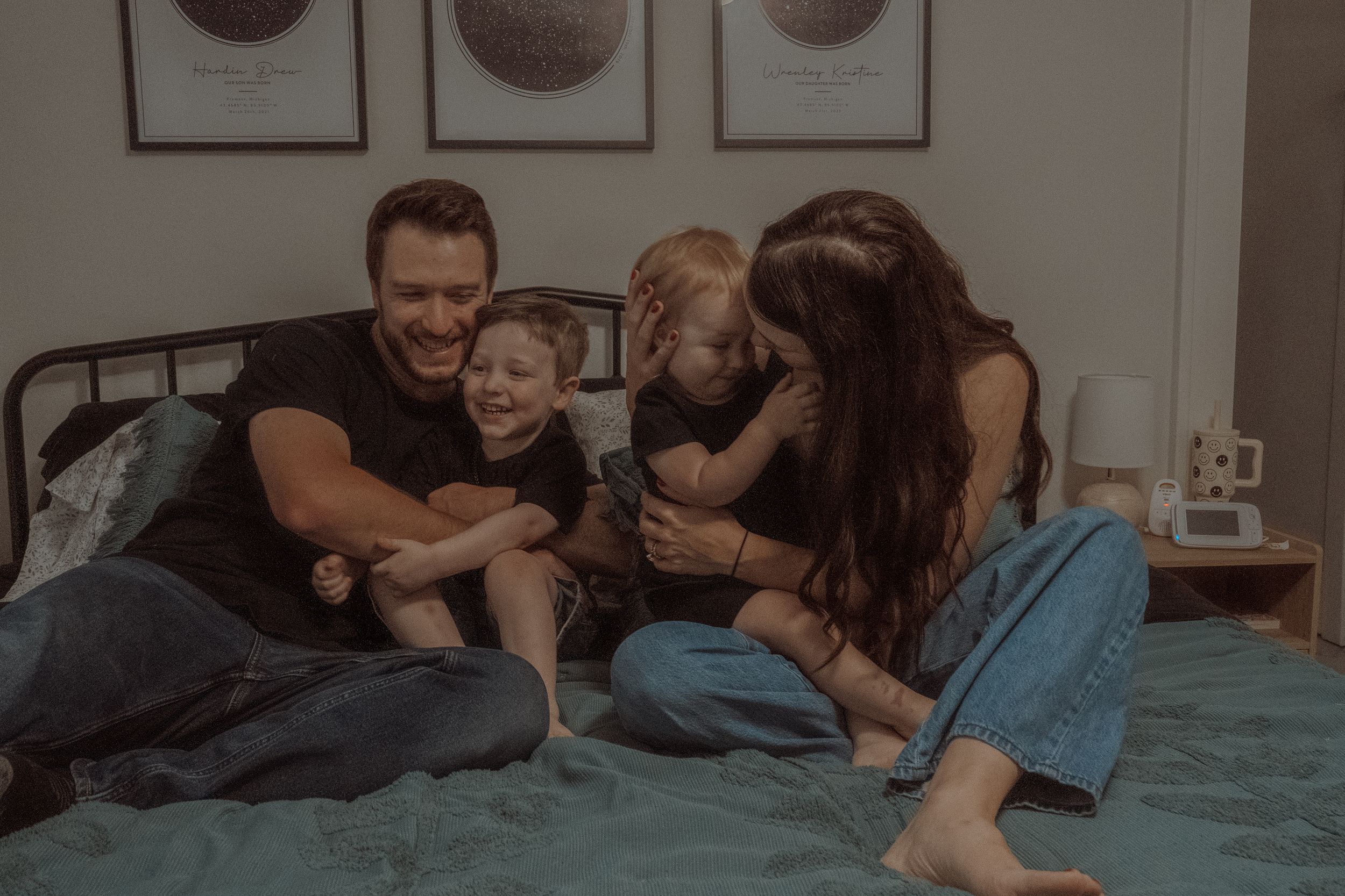 Family enjoying quality time together while sitting and laughing on a bed with decorative wall art.