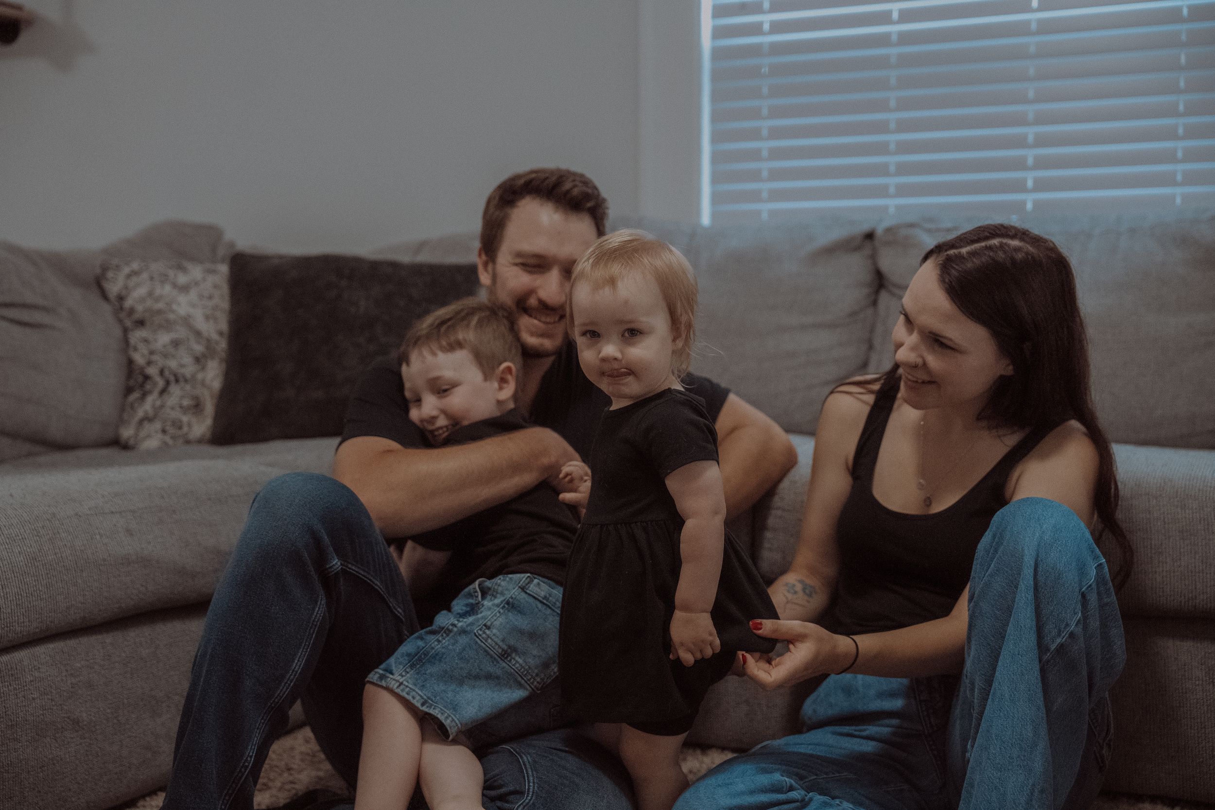 A family relaxes together on a gray couch in their living room during a casual afternoon at home.