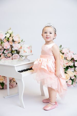 Sweet pink ballet-themed photoshoot with mini piano, floral arrangements and birthday cake on white backdrop.