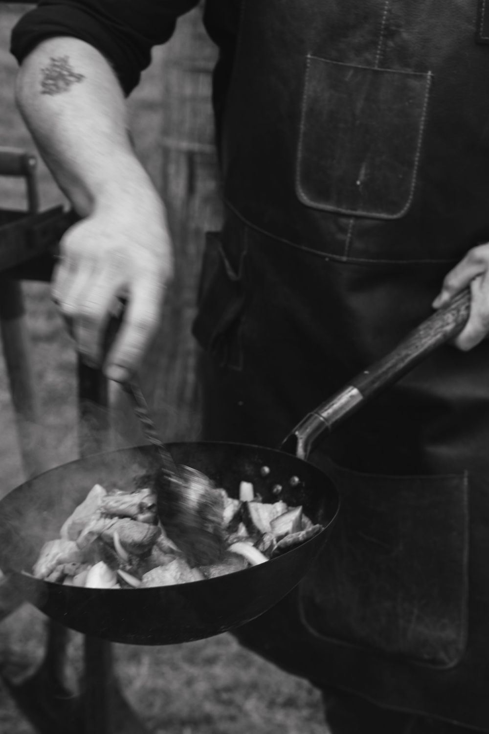 Black and white photo of hands cooking food in a cast iron skillet with steam rising.