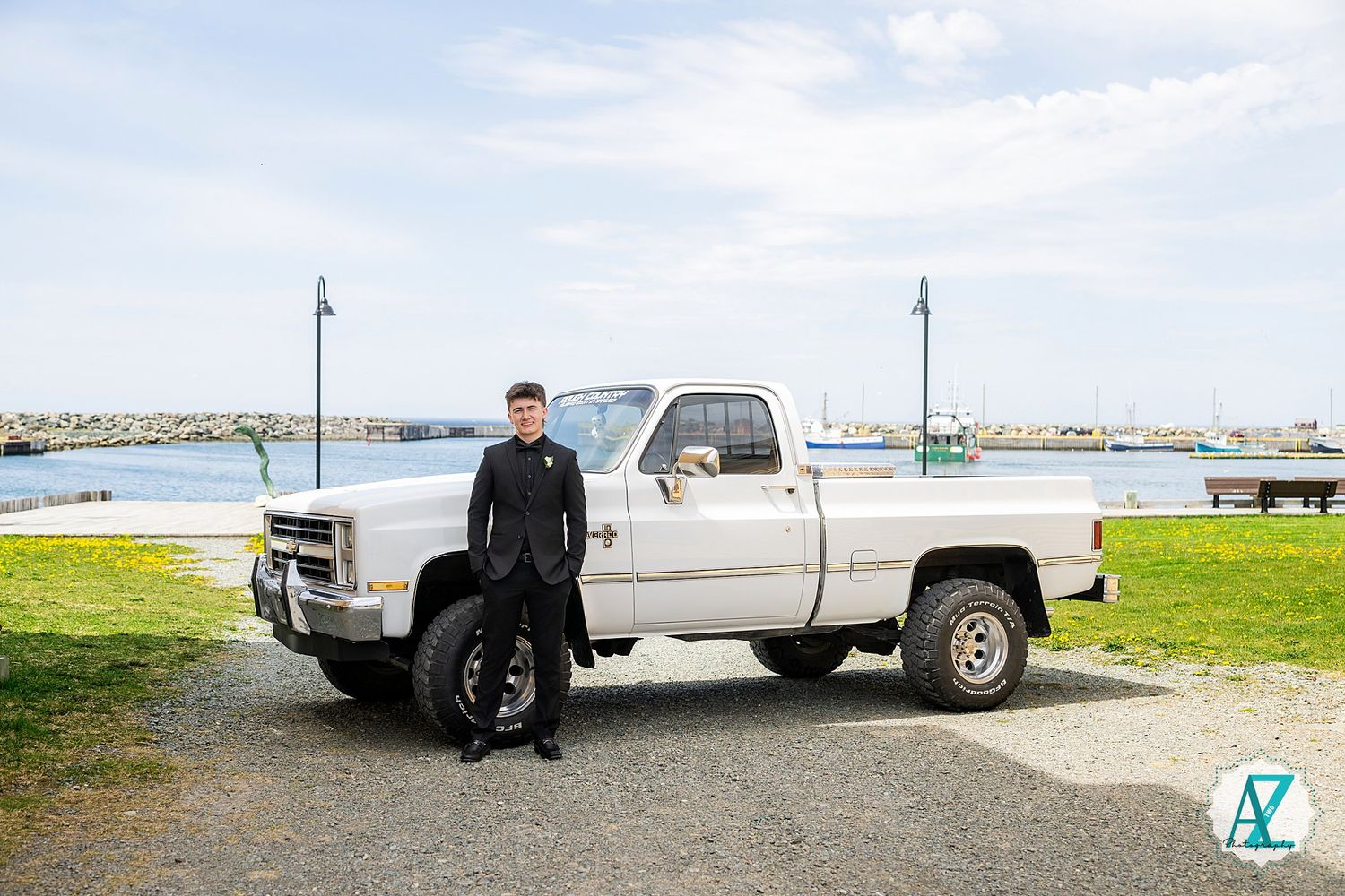 A classic white pickup truck parked by the waterfront with a person standing beside it in Maine.