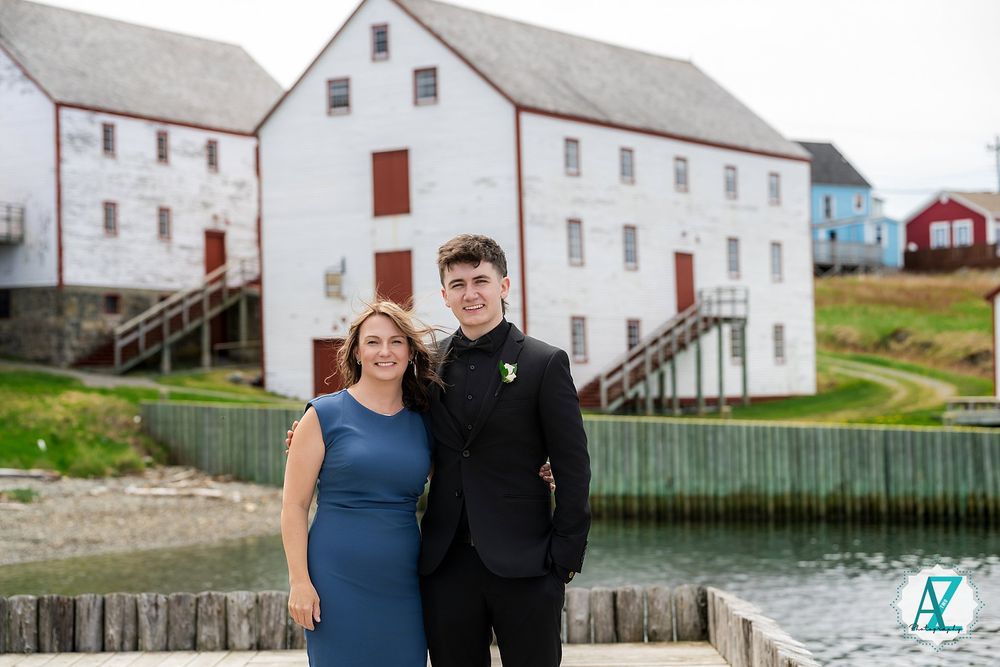 People standing by the historic white grist mill buildings at Trinity waterfront in Newfoundland.