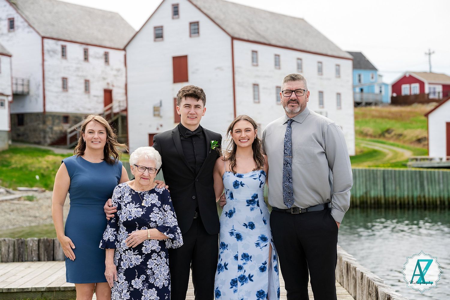 A group poses together on a wooden dock with classic white waterfront buildings and water in the background.