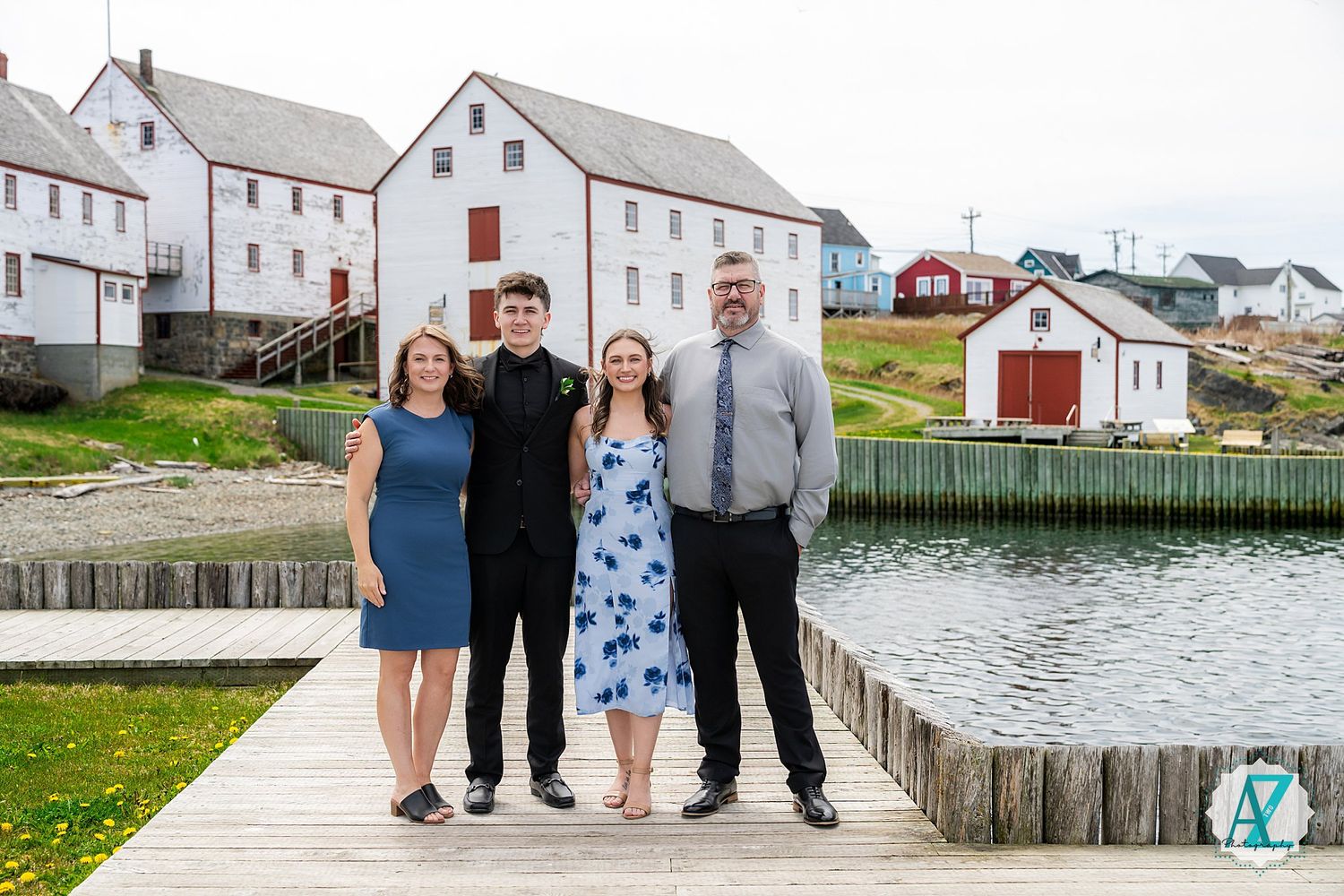 A group poses together on a wooden dock overlooking a harbor with white houses and buildings in the background.