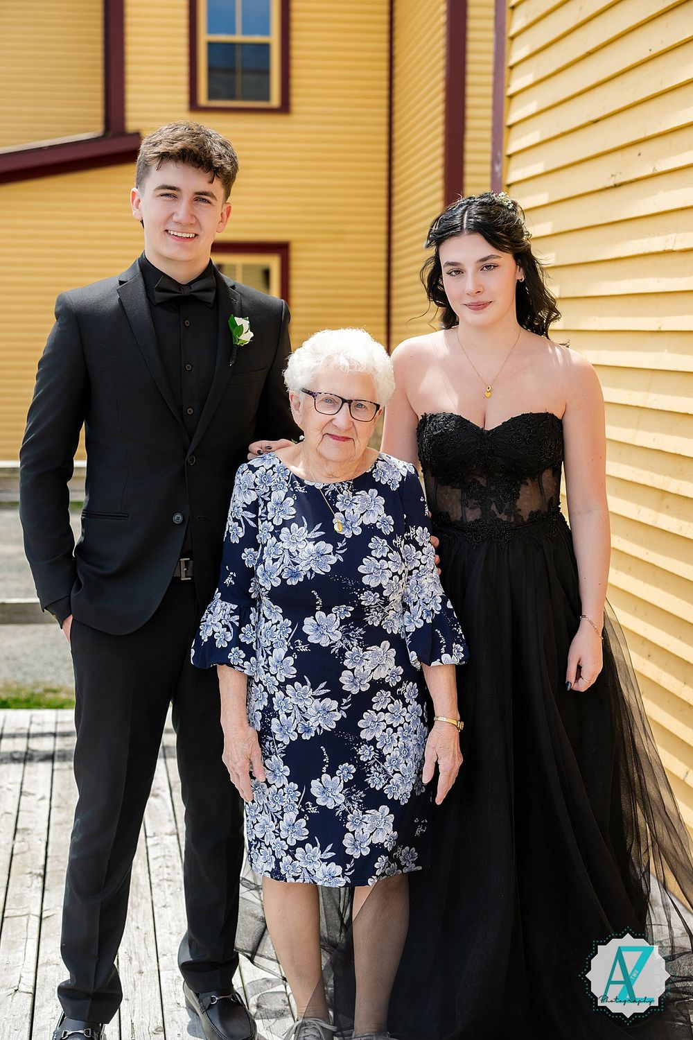 Three people pose for a formal photo against a bright yellow building exterior.