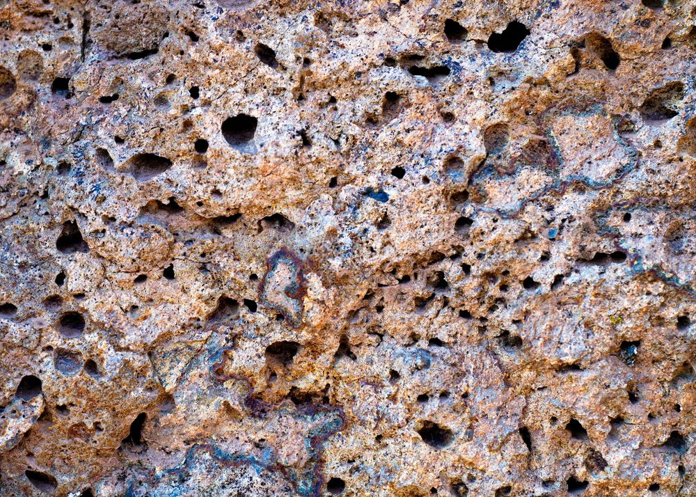 Close-up of porous volcanic rock surface with rough texture and scattered holes in brown and gray tones.