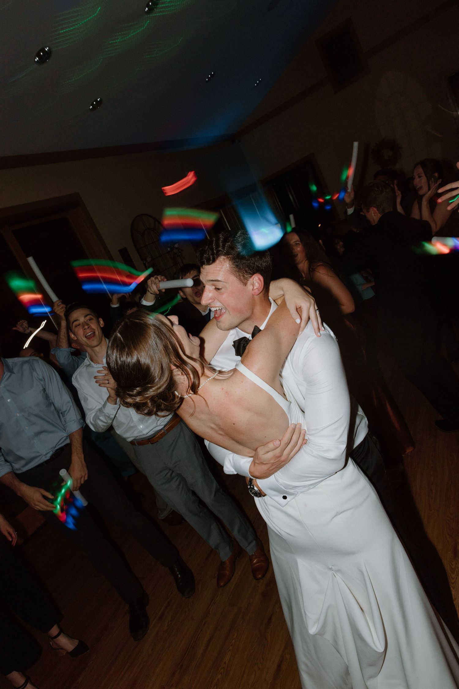 Wedding couple shares a romantic dance moment on the dimly lit dance floor with colorful lights in the background.