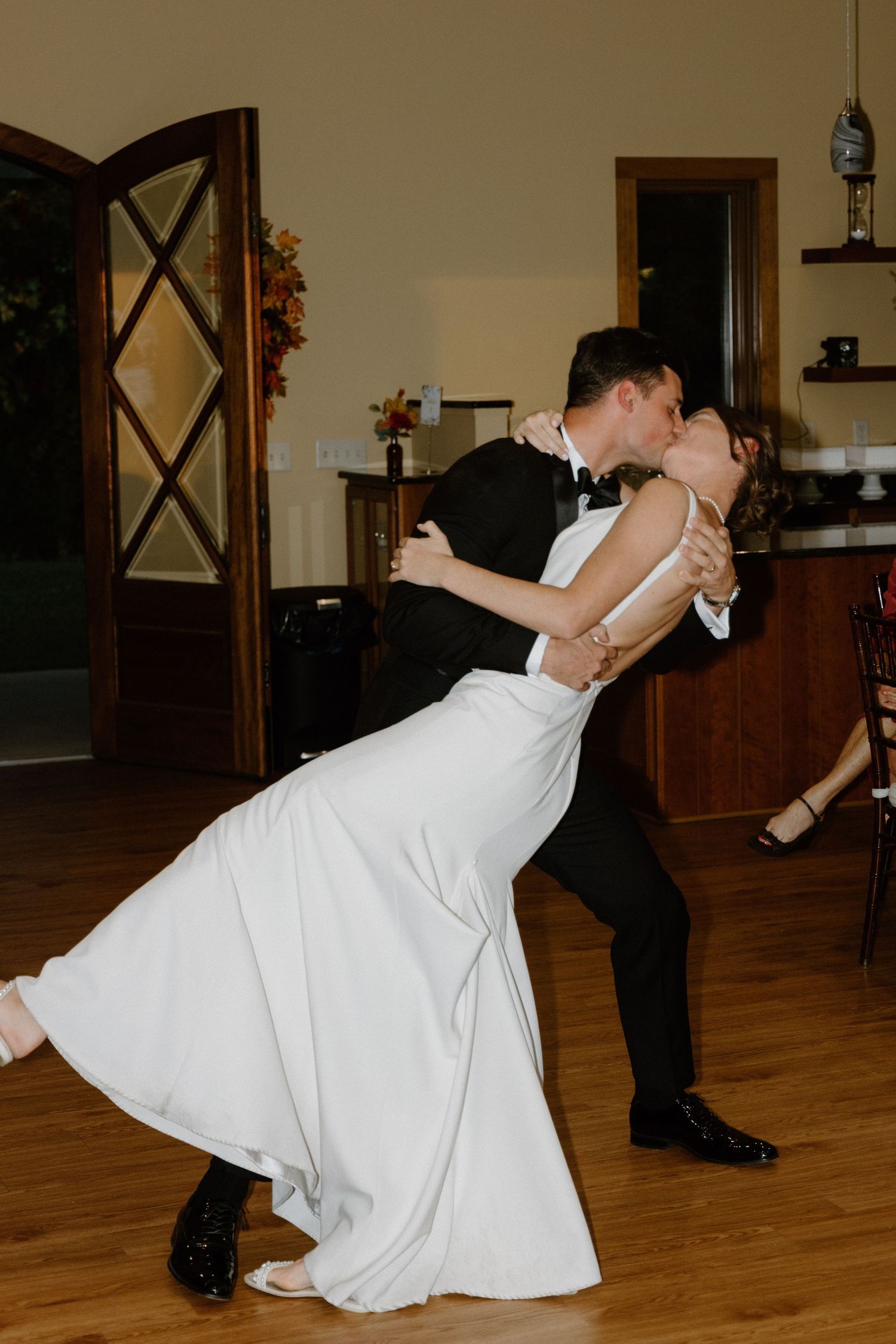 A couple performs a romantic dip while dancing in formal attire on a wooden floor indoors.