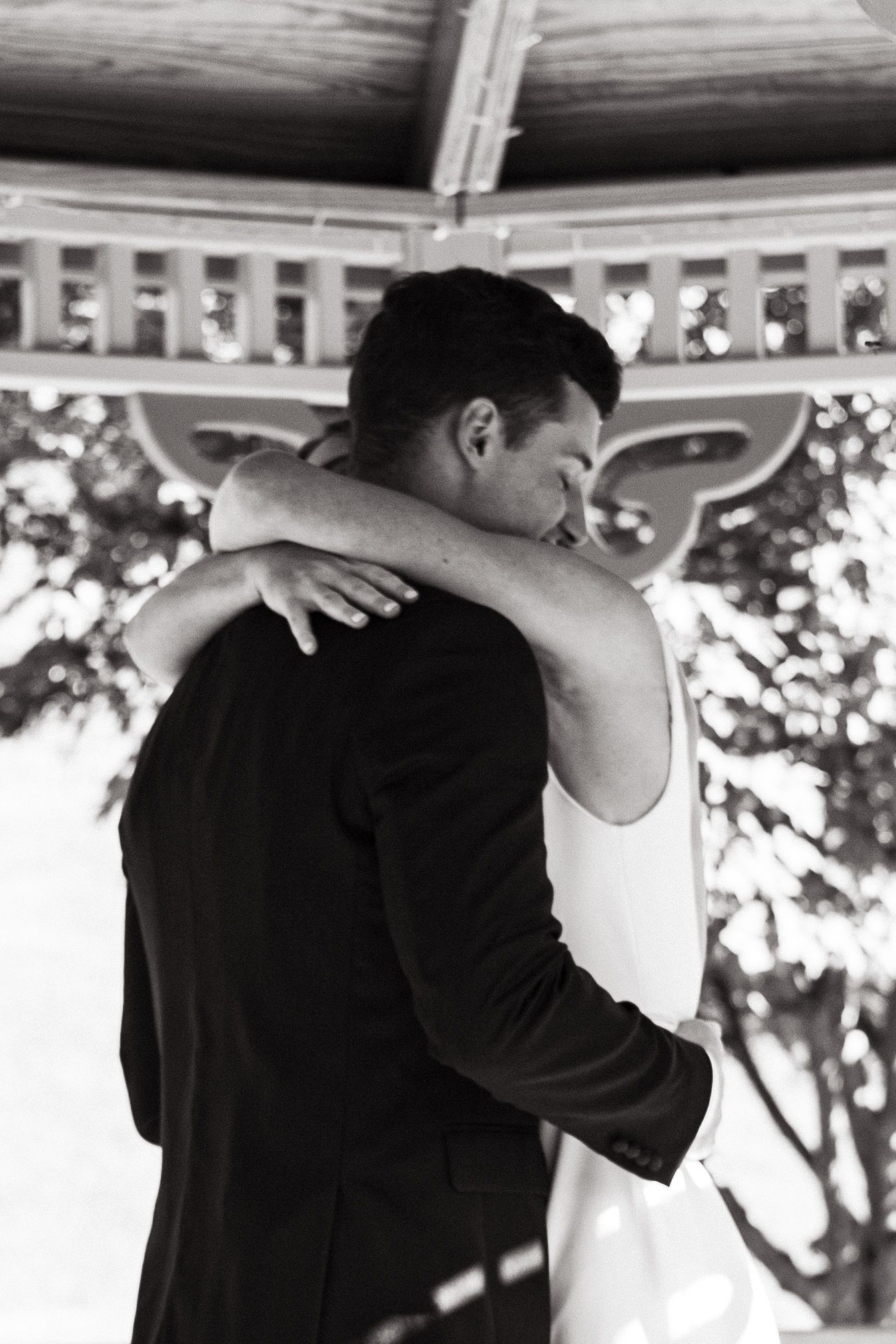 Black and white wedding photo showing romantic embrace between couple at an outdoor gazebo.