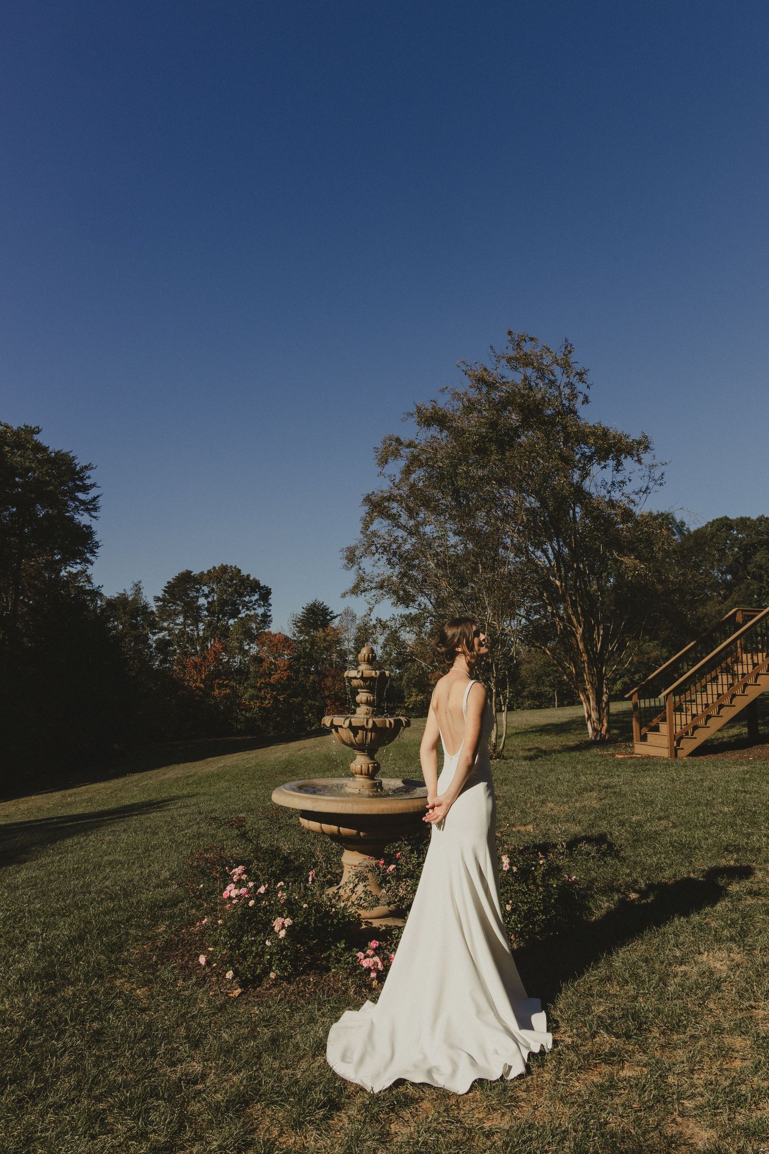 An elegant garden wedding photo shows a flowing white gown against a stone fountain and lush landscaping at dusk.