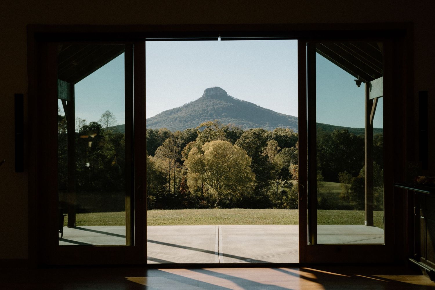 Mountain peak viewed through open glass windows with sunlit trees and countryside in the foreground.