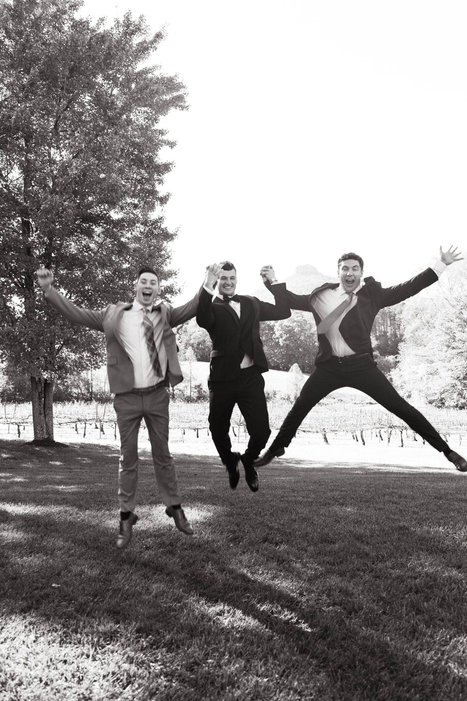 Black and white photos show a playful progression sequence of people jumping and leaping on a grassy hillside outdoors.