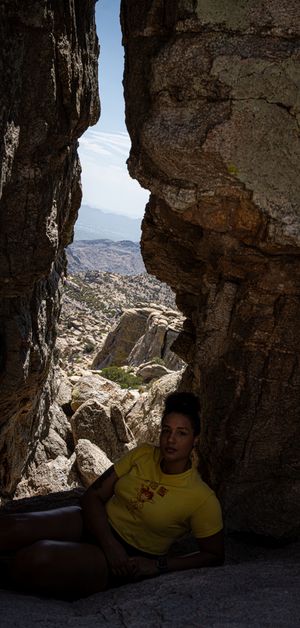 Adventure seeker resting in cave opening with dramatic mountain landscape view.
