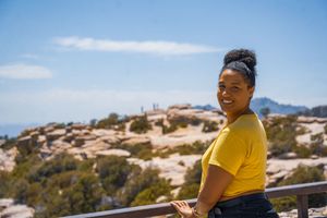Person in bright yellow t-shirt smiling while enjoying scenic mountain overlook on clear sunny day.