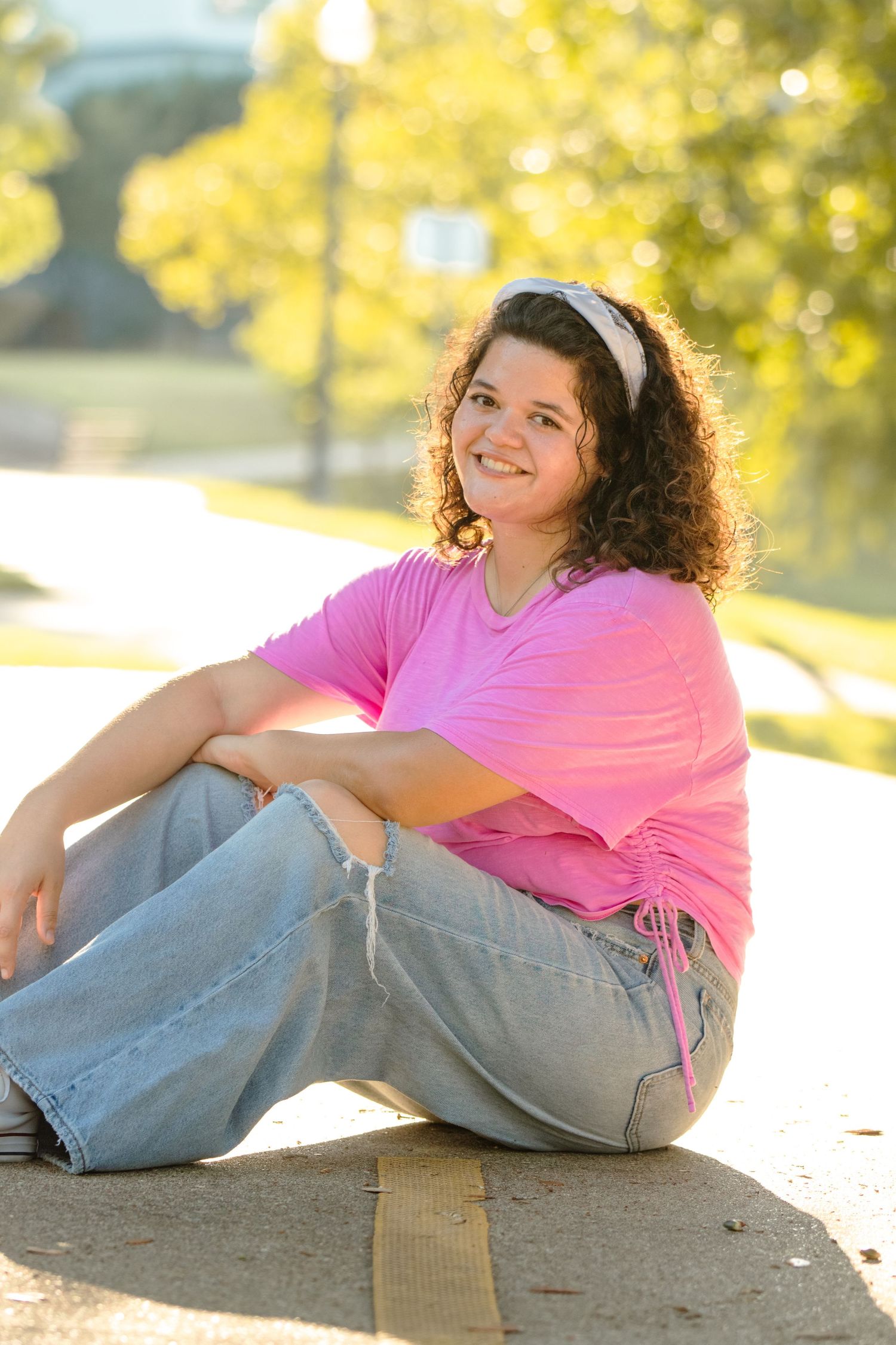 Casual portrait series in bright sunlight showing someone in pink shirt and jeans sitting on ground with curly hair.