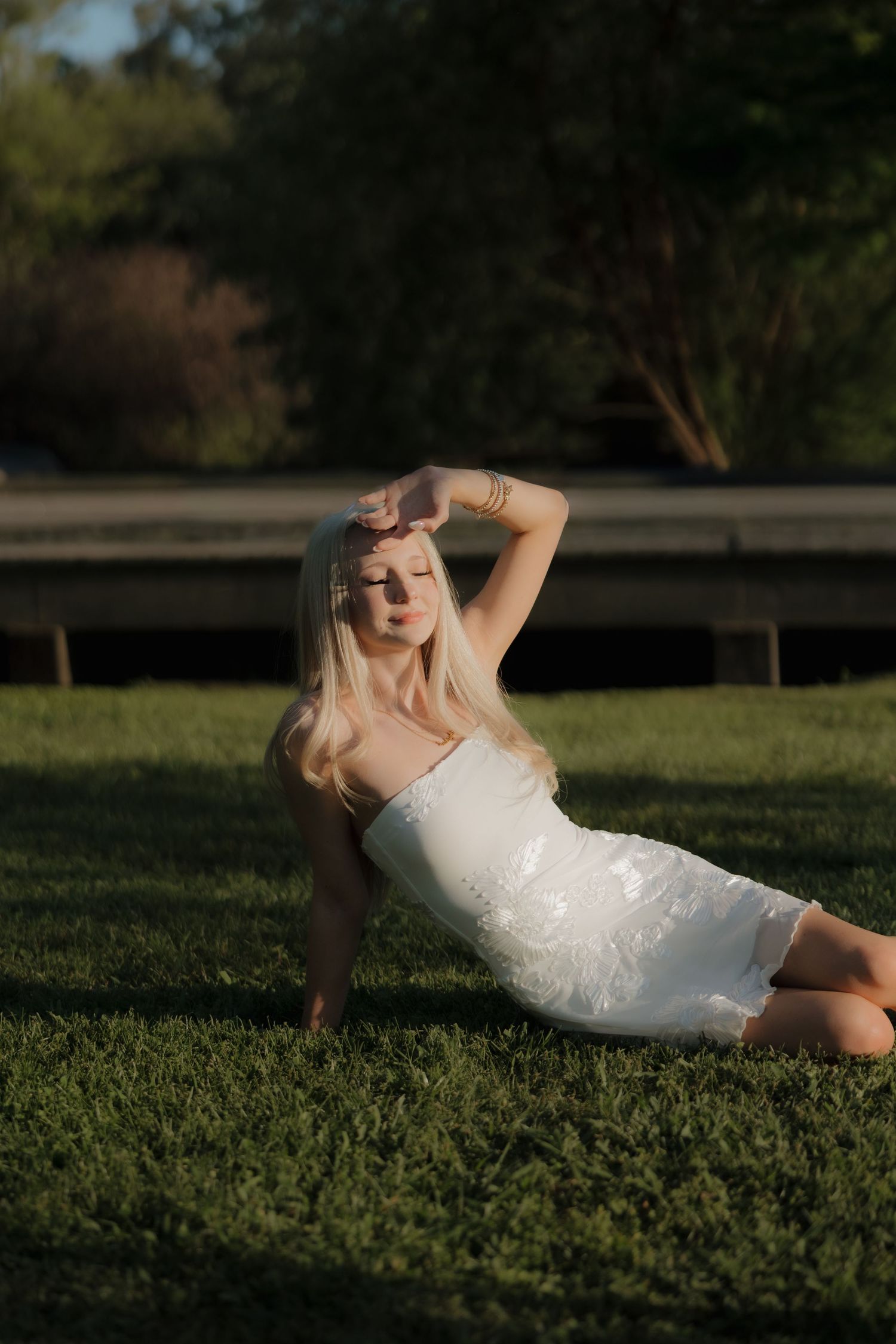 Close-up view of a graduation cap and white dress with beige heels on concrete ground.