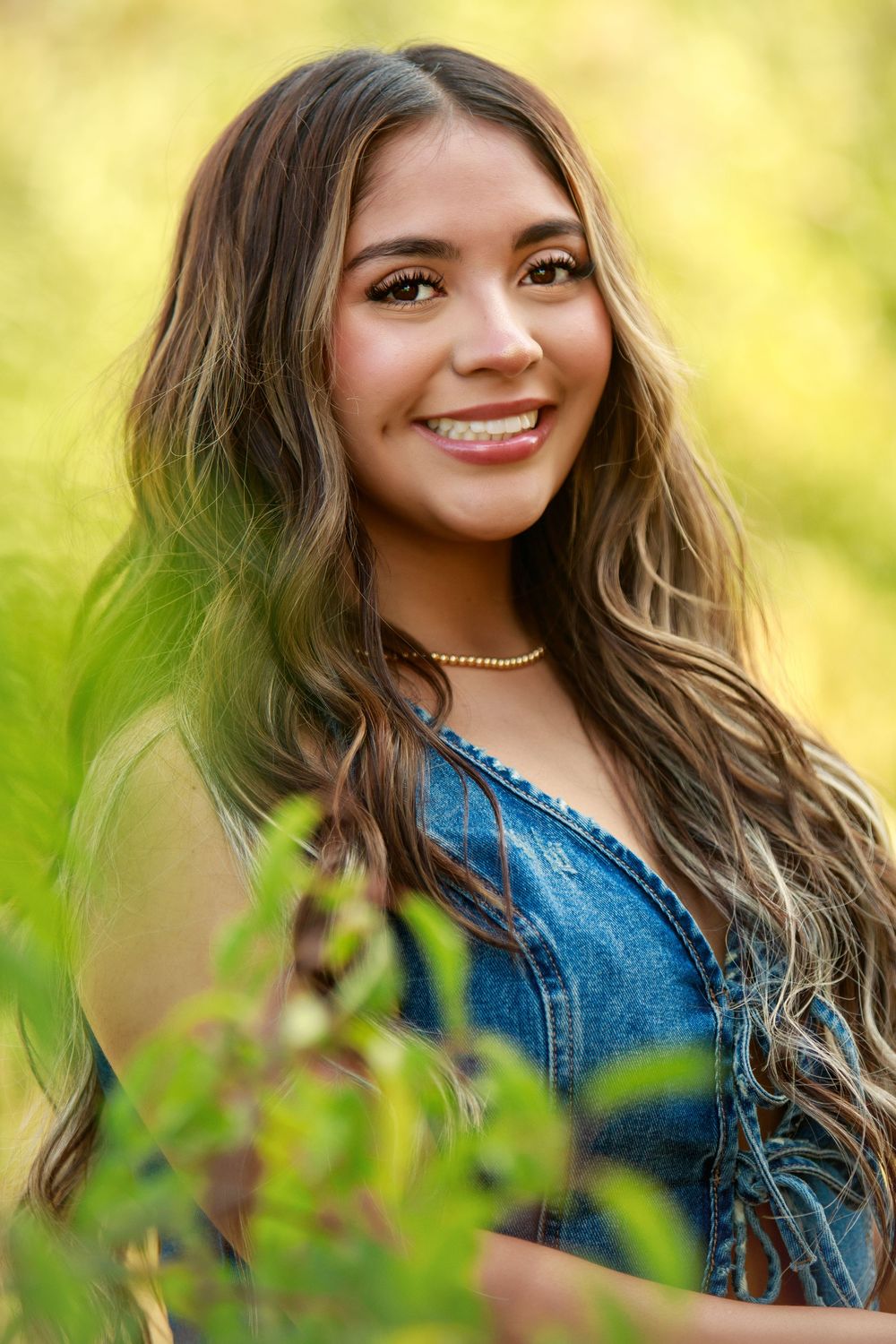 Outdoor portrait featuring wavy ombre hair, denim top and choker necklace against a soft yellow-green natural background.