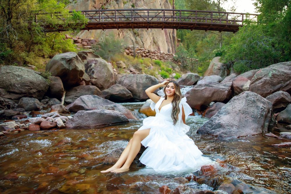 Beautiful scene of someone in a white dress sitting on rocks by a mountain stream with rustic bridge overhead.