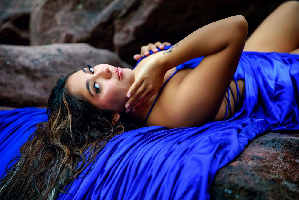 Woman in vibrant blue dress poses elegantly on rocks during outdoor photo session.