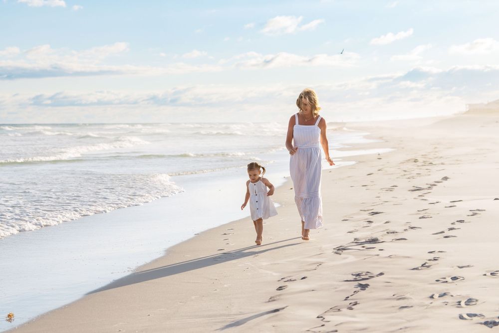 Children stroll along a serene beach in white clothing while waves gently roll onto the sandy shore at sunset.