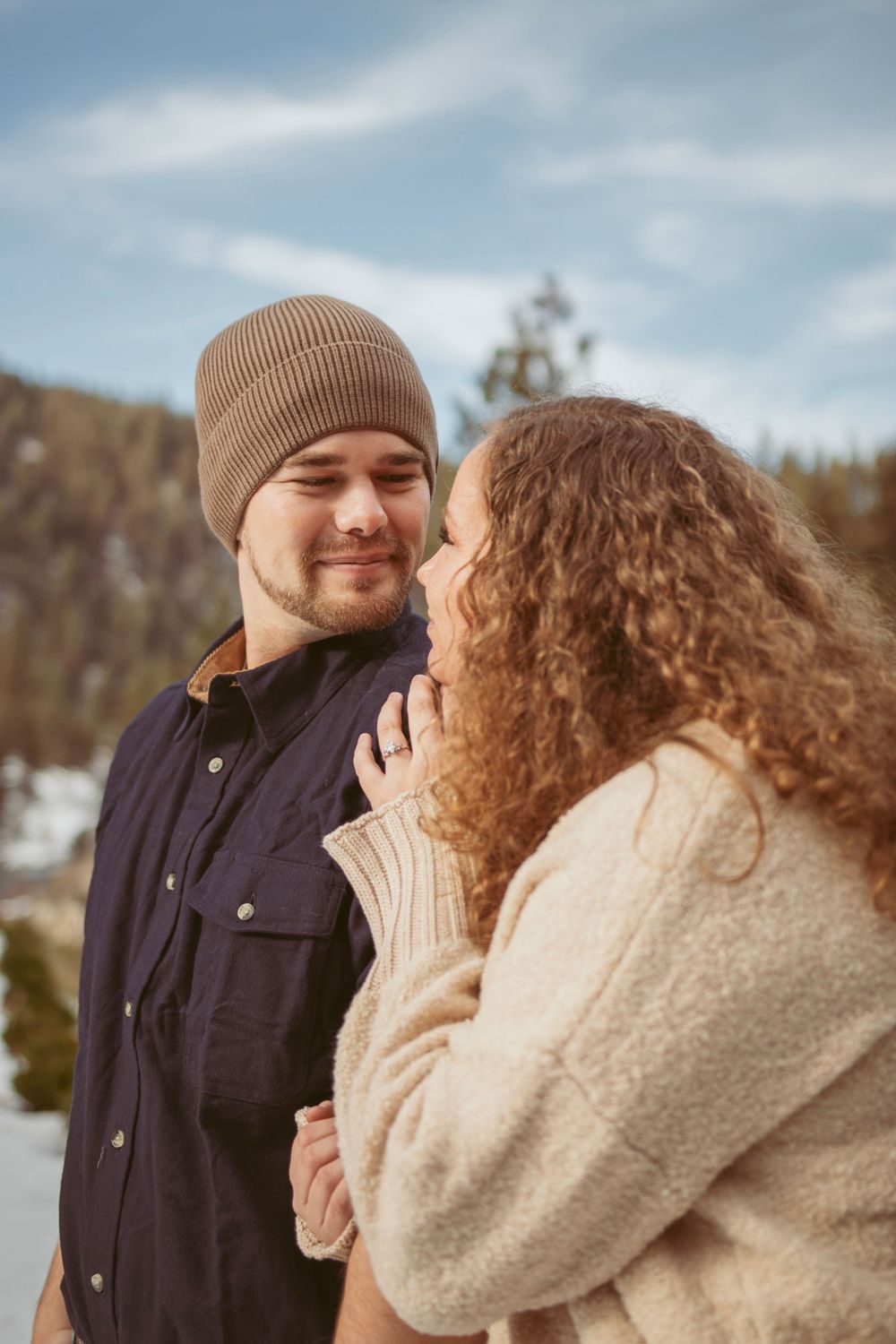 A romantic winter engagement photo series showing a cozy couple embracing outdoors in warm sweaters against a snowy landscape.
