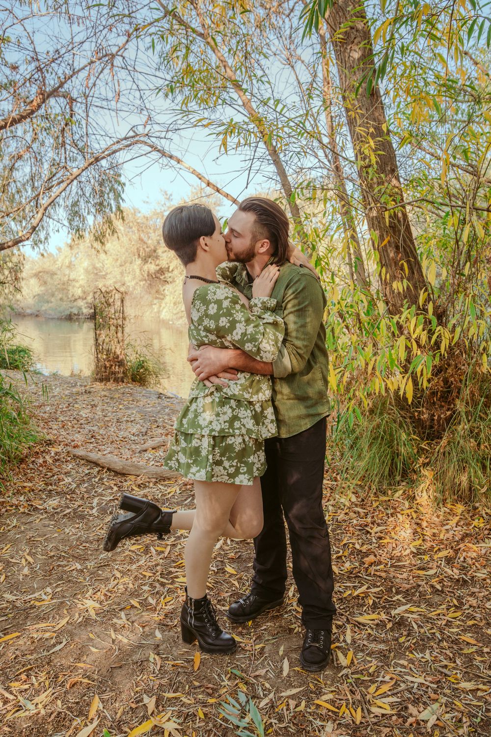Intimate romantic scene with a couple embracing on a dirt path beside autumn trees and a tranquil lake.