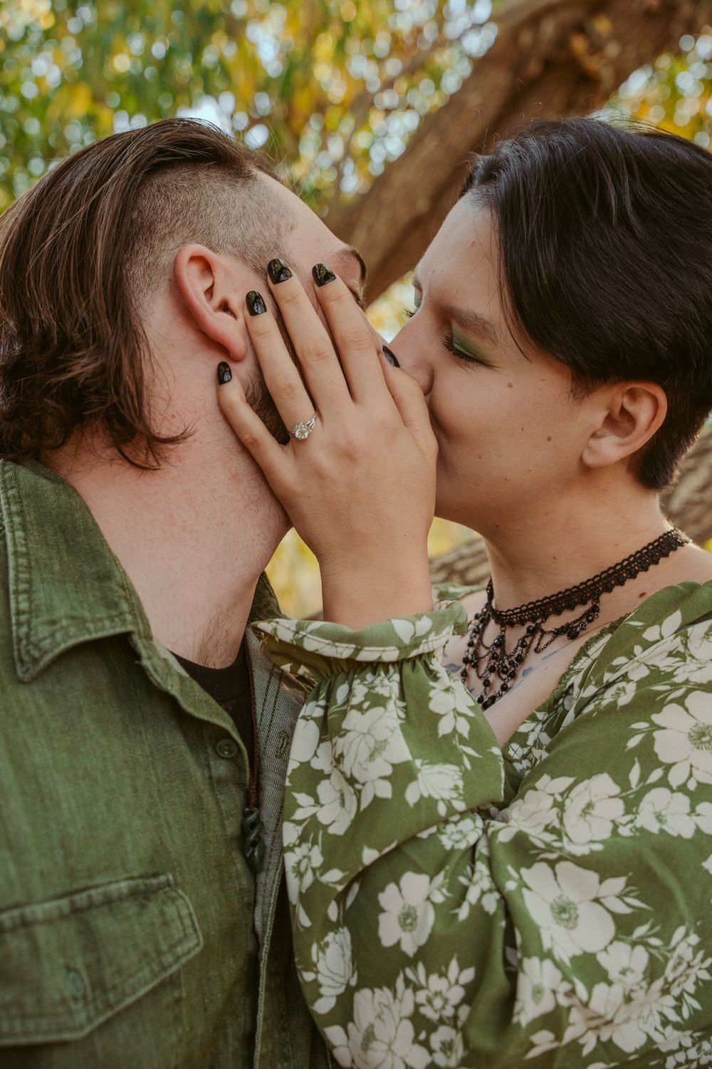 A couple shares an intimate moment outdoors with black nail polish visible and a floral print shirt.
