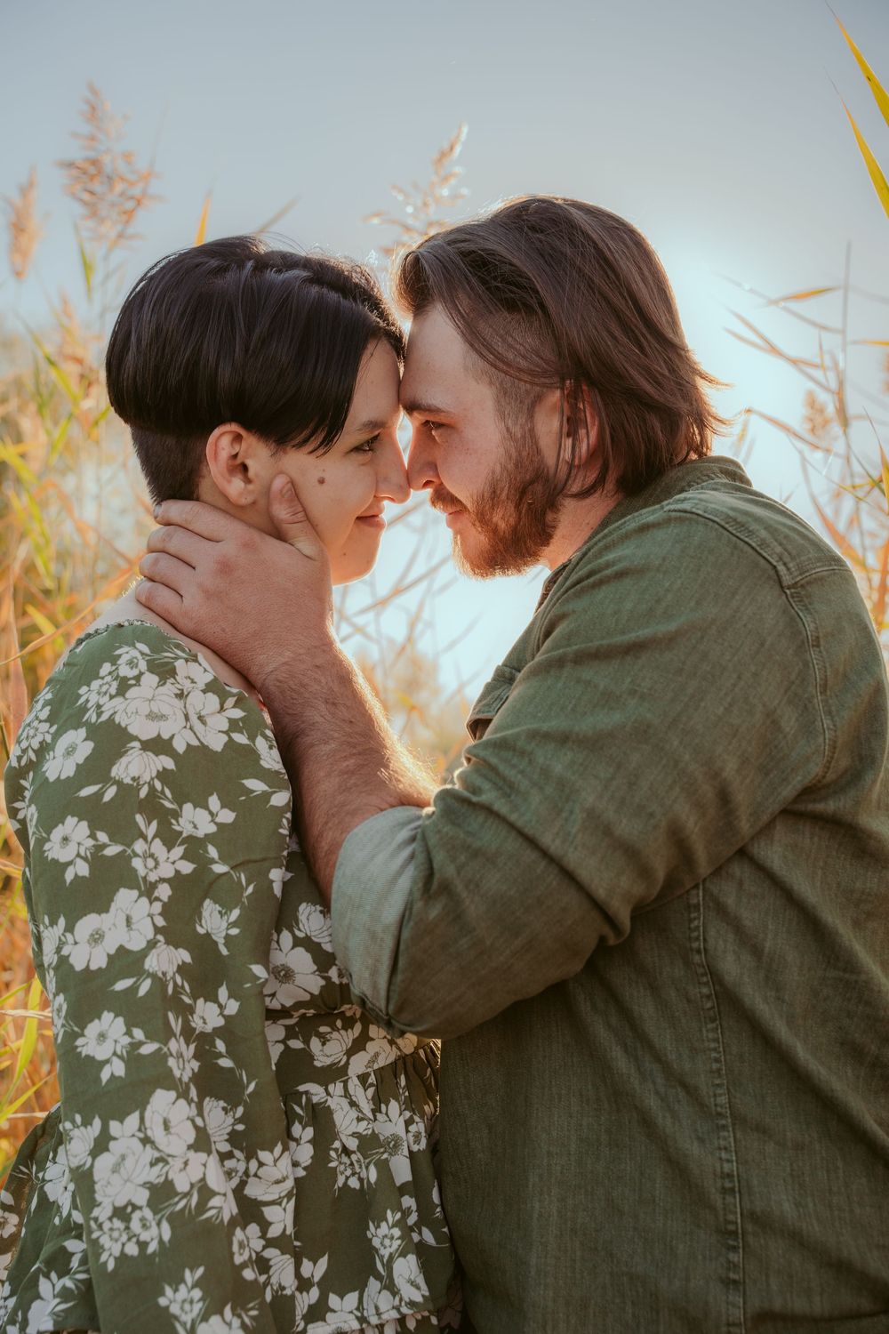 Intimate couple sharing tender moment in golden sunlit field of tall grass and autumn flora.