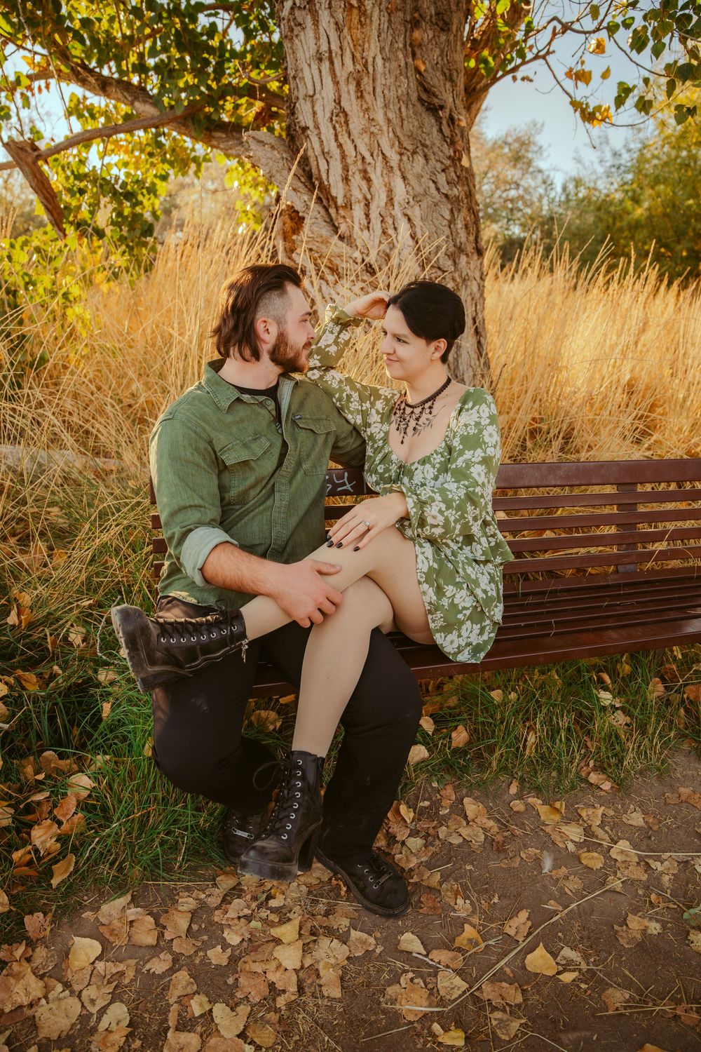 A couple shares an intimate moment on a wooden bench amid fall foliage and golden sunlight.