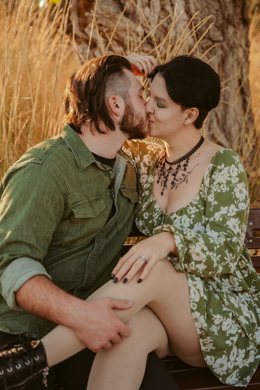 A romantic couple embraces and kisses intimately during a sunset photoshoot in a field of golden grass.
