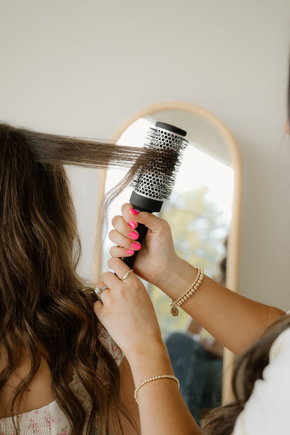 Close-up shots of hands using round brush while styling dark hair against light background.