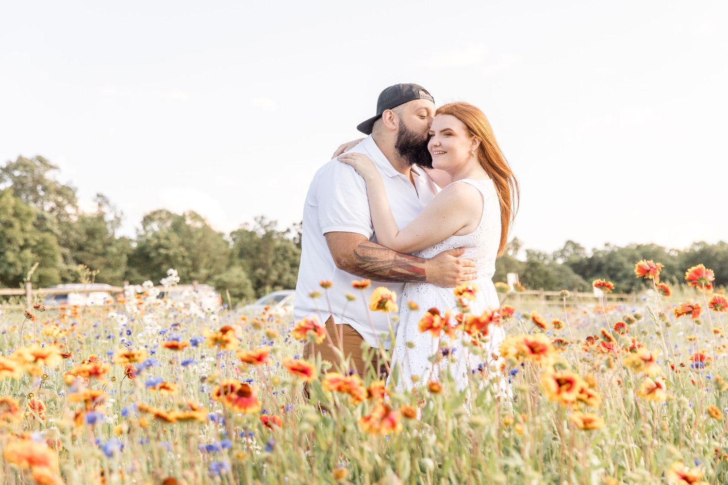 A couple sits together in a sunlit wildflower meadow with yellow flowers during golden hour.