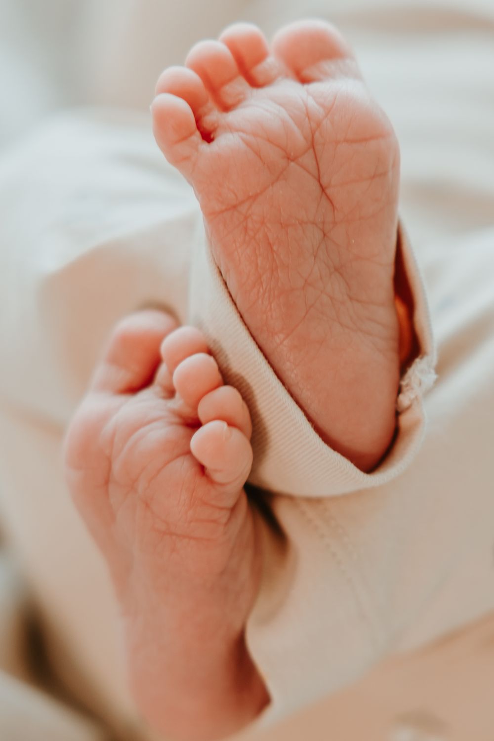 Close-up series showing tiny wrinkled baby feet against a soft white blanket background.