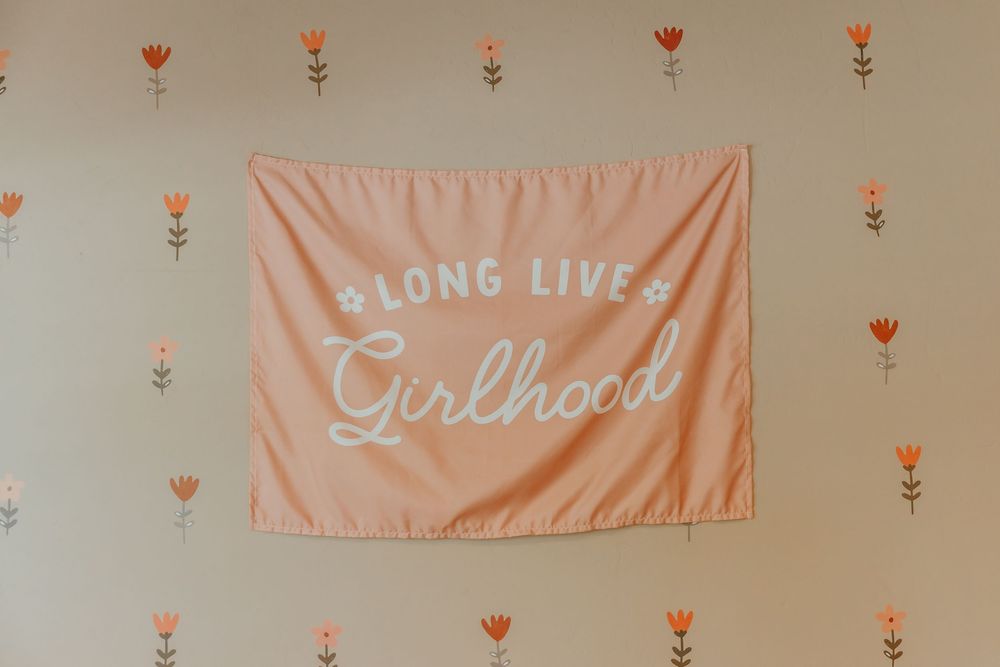 A series of soft pink banners with text hang against a beige wall decorated with small floral details.